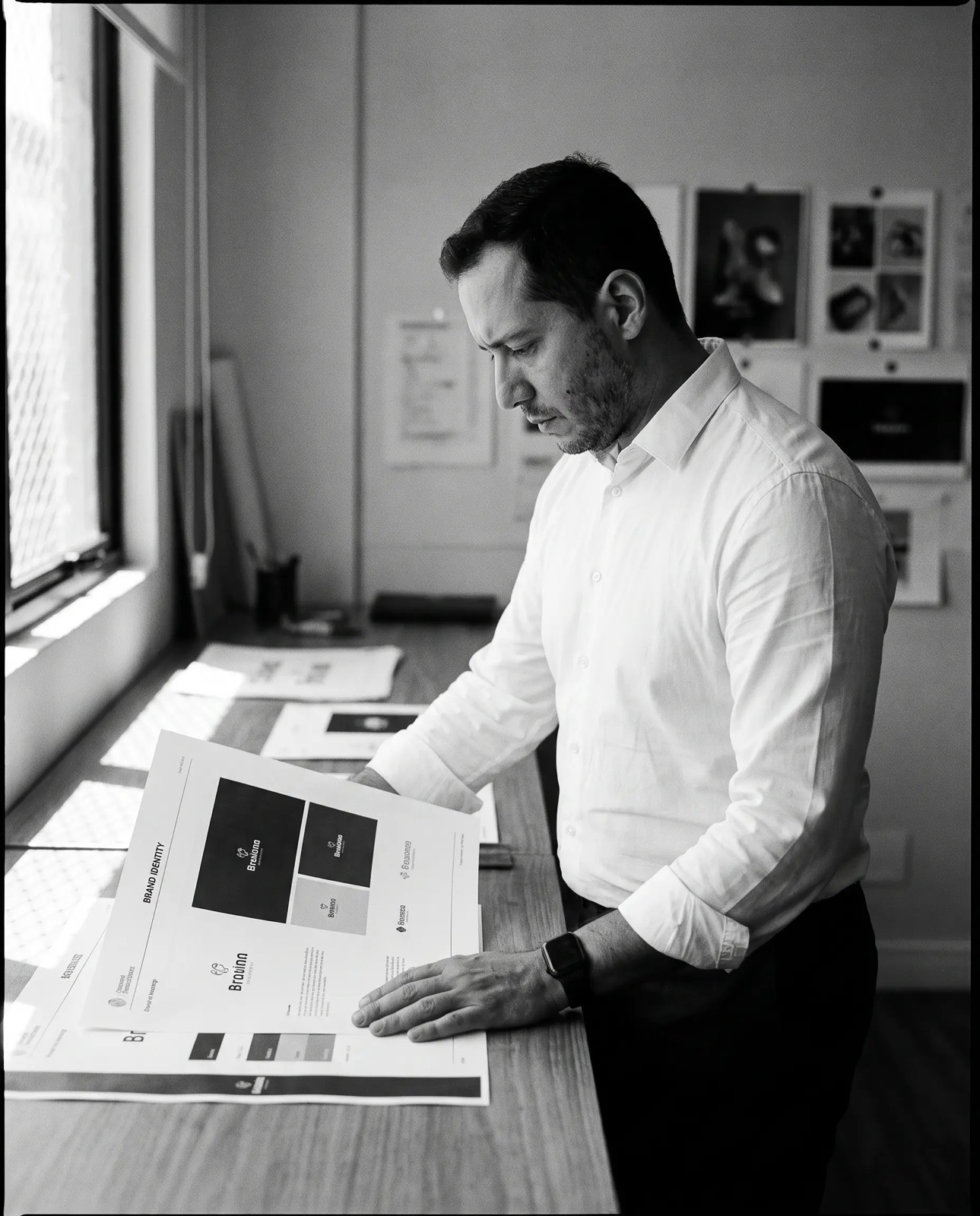 Fabio Pito in profile, reviewing printed brand identity sheets at the studio workbench, in black and white